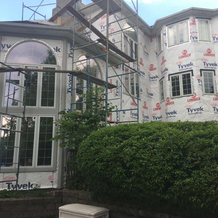 House undergoing exterior renovation with scaffolding and protective Tyvek wrap