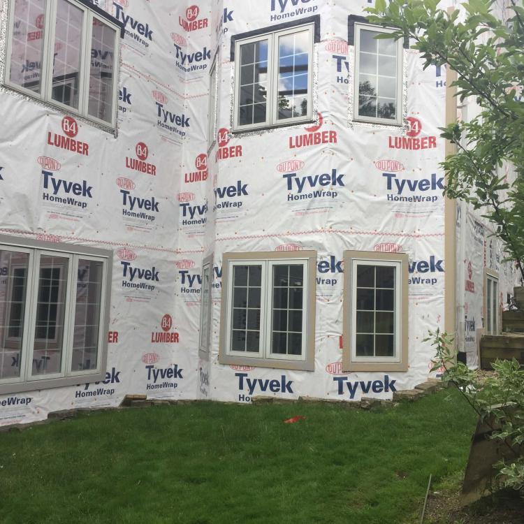 House undergoing siding repair with scaffolding and protective Tyvek wrap