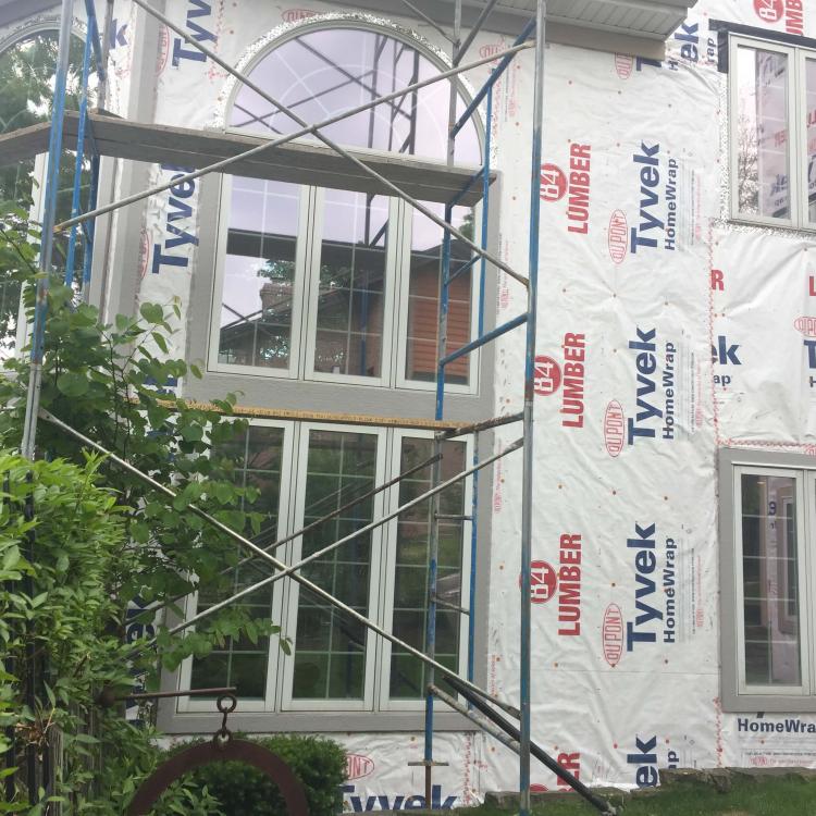 House siding repair with scaffolding and protective wrap.