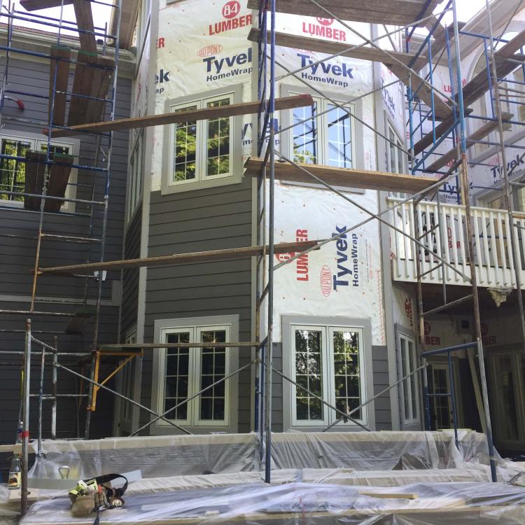 House undergoing siding repair with scaffolding and Tyvek wrap.