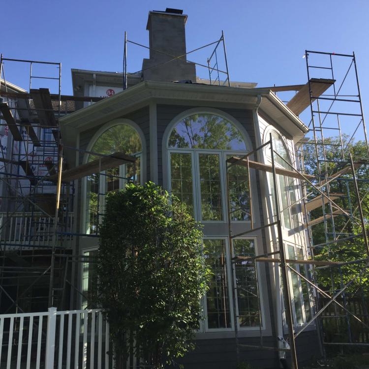 House undergoing exterior renovation with scaffolding and Tyvek, focusing on a large arched window