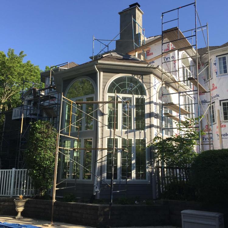 House undergoing exterior renovation with scaffolding, focusing on a large arched window