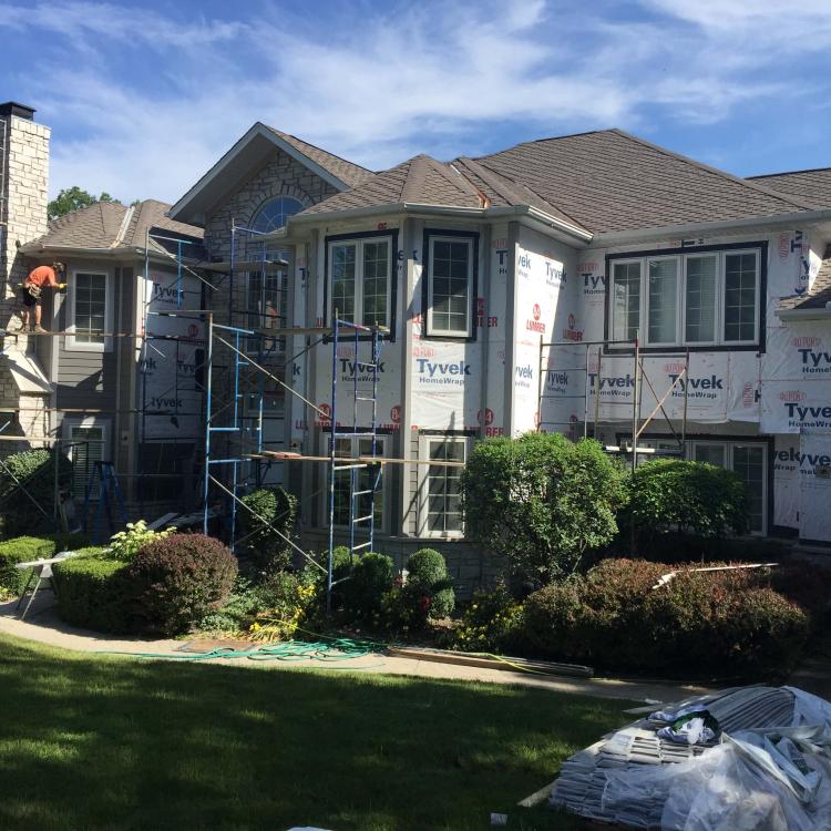 Siding repair project in progress. Workers are visible on the scaffolding.