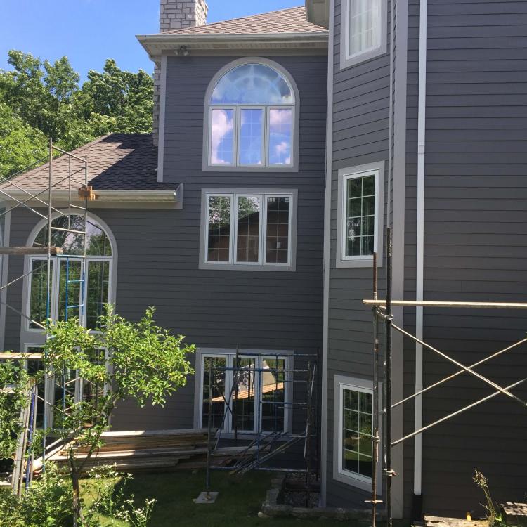 House undergoing siding repair with scaffolding, highlighting the gray siding and arched window