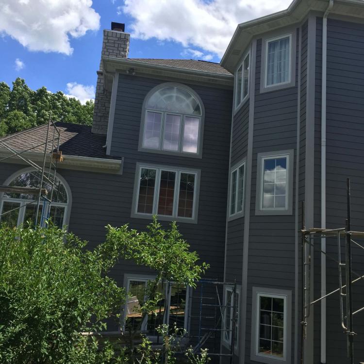 House undergoing siding repair with scaffolding, showcasing the gray siding and arched windows