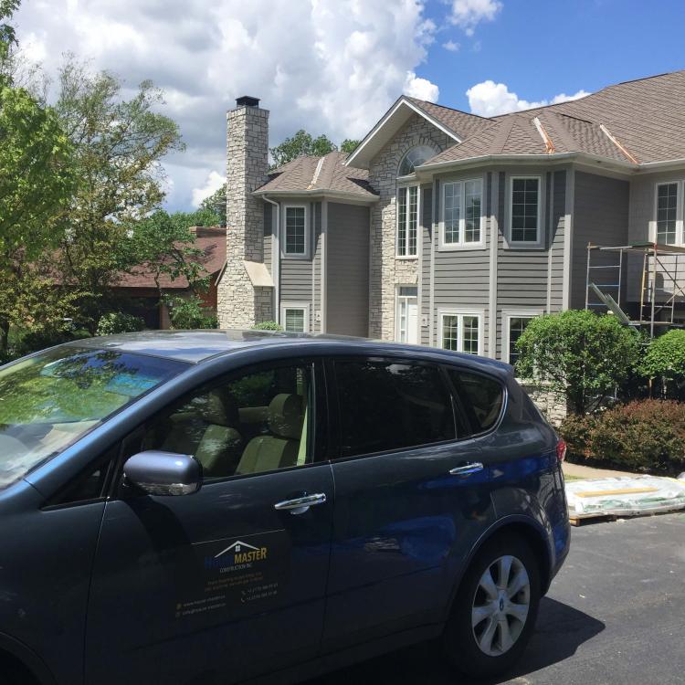 House exterior painting in progress: painters' car parked in driveway.