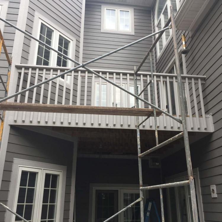 House undergoing siding repair, with scaffolding set up near a balcony