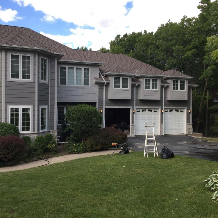 House with newly repaired siding, featuring a gray exterior and stone accents.