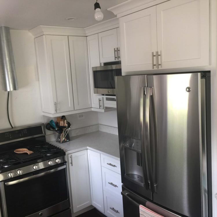 Kitchen remodel complete: white cabinets, quartz countertops, stainless steel fridge.