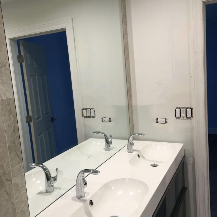 White double vanity with sleek chrome faucets and large mirror in renovated bathroom.