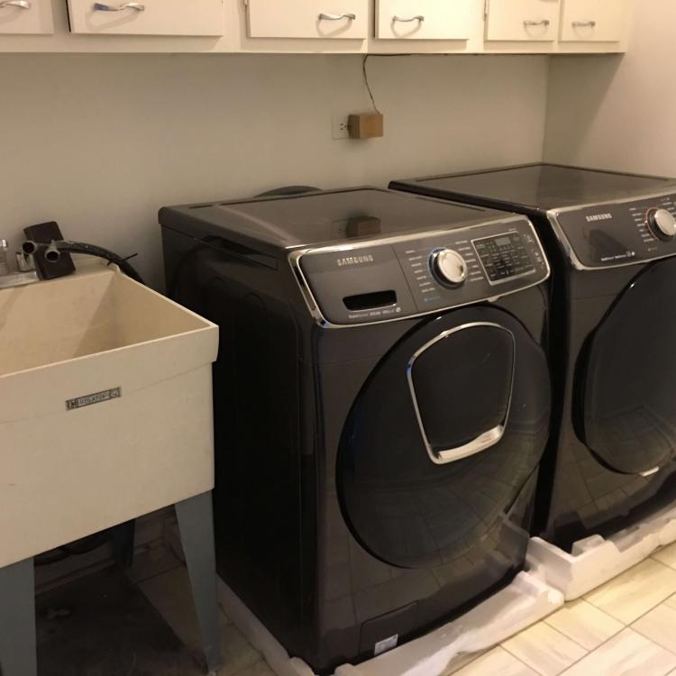 Completed laundry room renovation with new Samsung appliances and white cabinets.