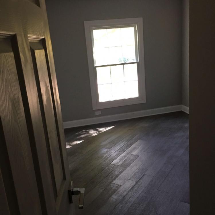 Completed bedroom renovation with gray walls, a white window frame, and dark wood floors.