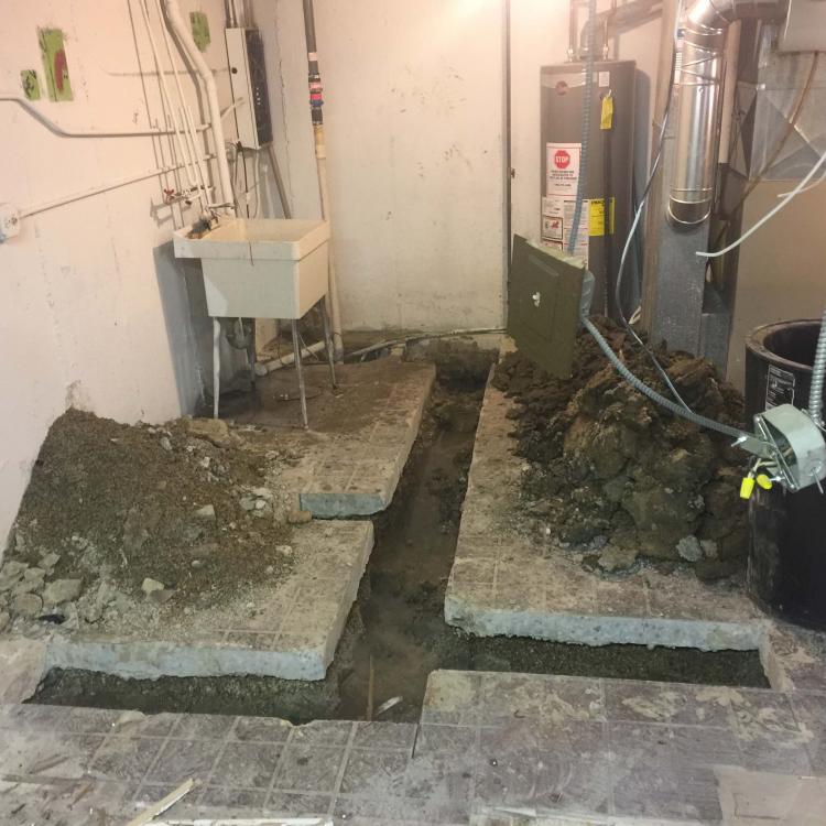 A basement with exposed pipes and broken concrete due to ongoing construction or renovation work