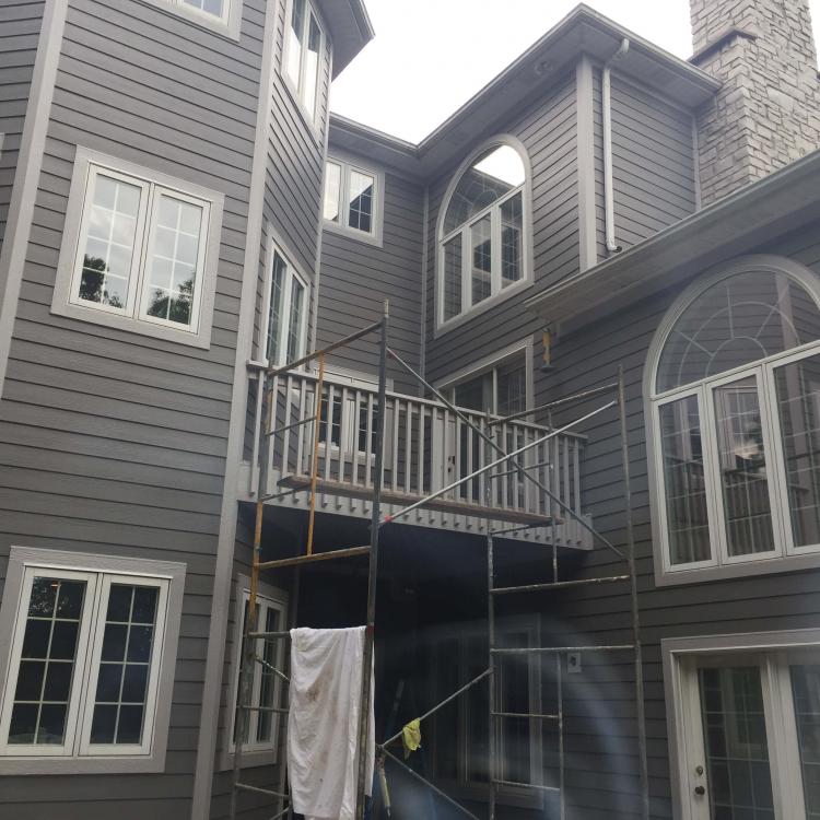 A two-story house with gray siding and white windows while siding or stucco repair work