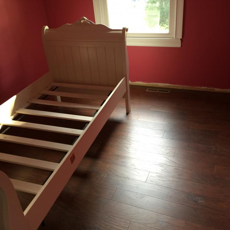 A bedroom with a bed frame and dark wood floors