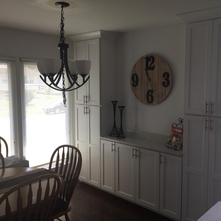 A modern kitchen with white cabinets, a round wooden clock, and a dining table with chairs