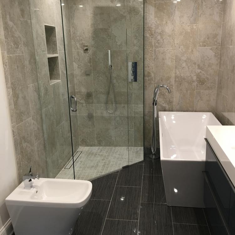 A modern bathroom with a large glass shower, a freestanding bathtub, and black tile flooring.