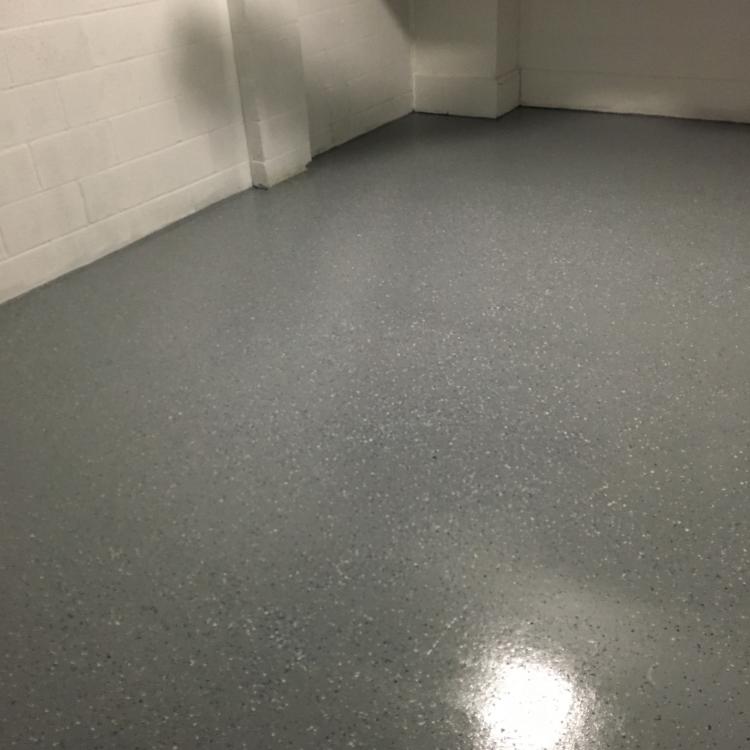 A finished basement floor with a smooth, gray epoxy coating.