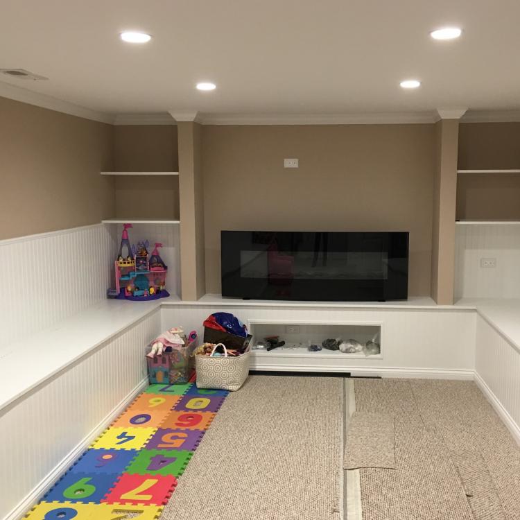 A finished basement room with a fireplace, built-in seating, and a play area for children