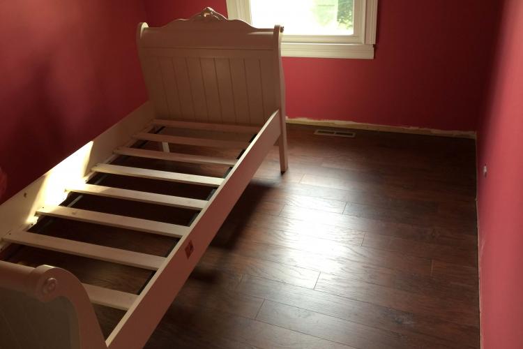 Completed laminate flooring installation: Room with new flooring and a bed.