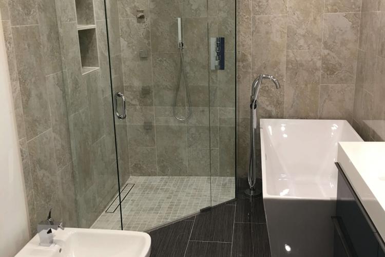 Modern bathroom renovation with glass shower, standalone tub, bidet, and dark tiled floor