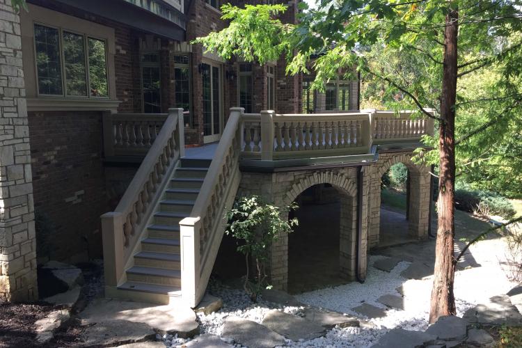 A large, two-story brick house with a patio and a curved staircase leading to a deck