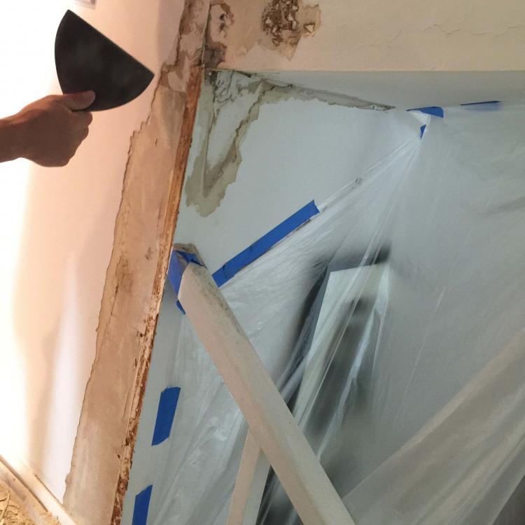 Interior painting preparation: worker scraping damaged wal