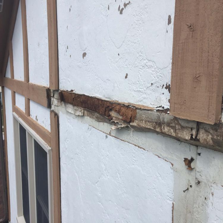 A house with damaged stucco and exposed wood, indicating the need for wall repair