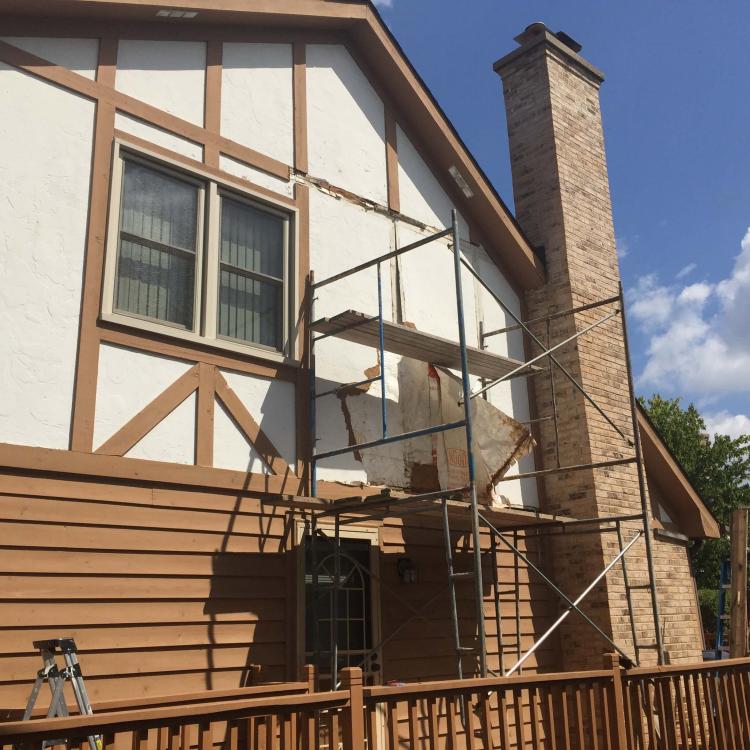 A house with damaged stucco and scaffolding set up for wall repair work.