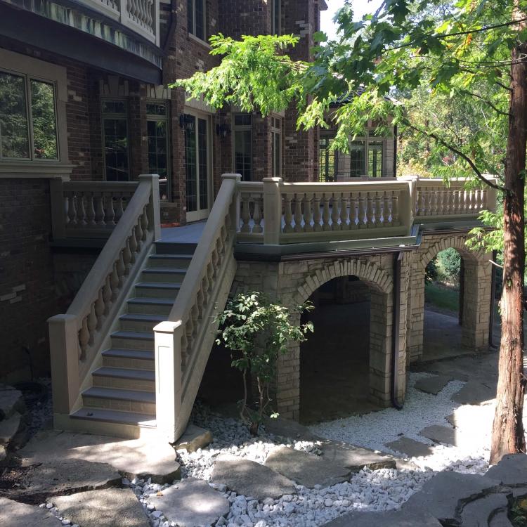 A large, two-story brick house with a patio and a curved staircase leading to a deck