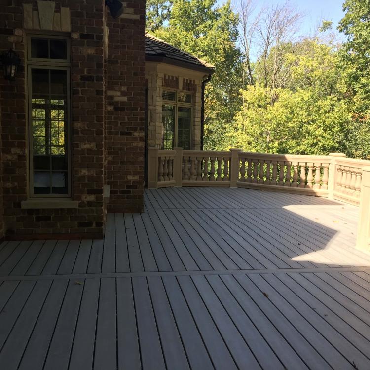 A large, replaced deck with gray composite planks and ornate stone railings.