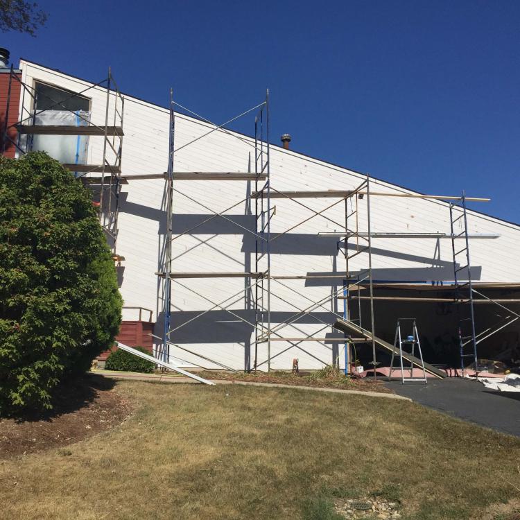 A house with scaffolding set up for exterior painting after siding replacement works.