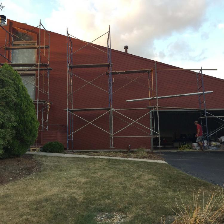 A house with scaffolding surrounding during ongoing painting work after siding replacement.