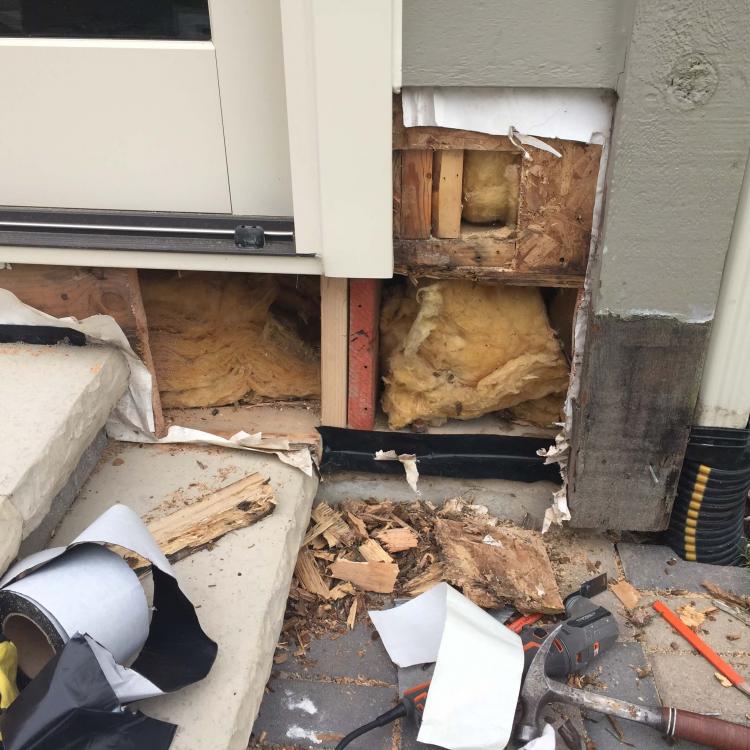 A damaged house exterior with exposed wood and insulation, indicating siding repair works.